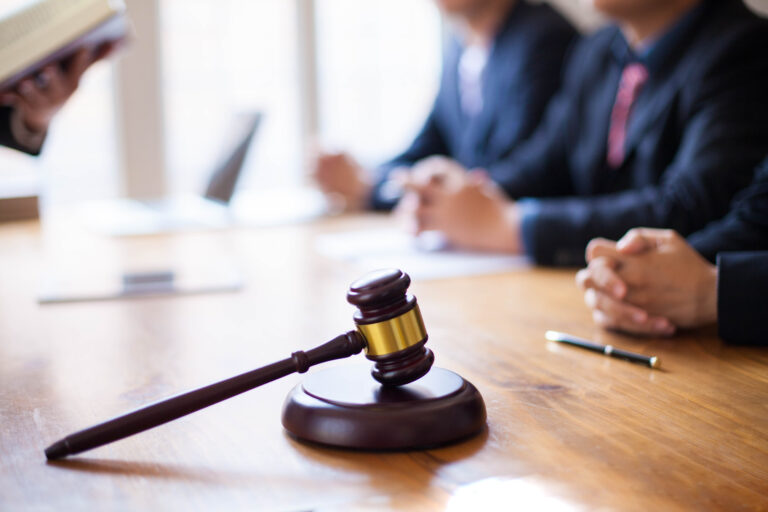 Richterhammer auf einem Tisch mit drei Menschen mit Anzug